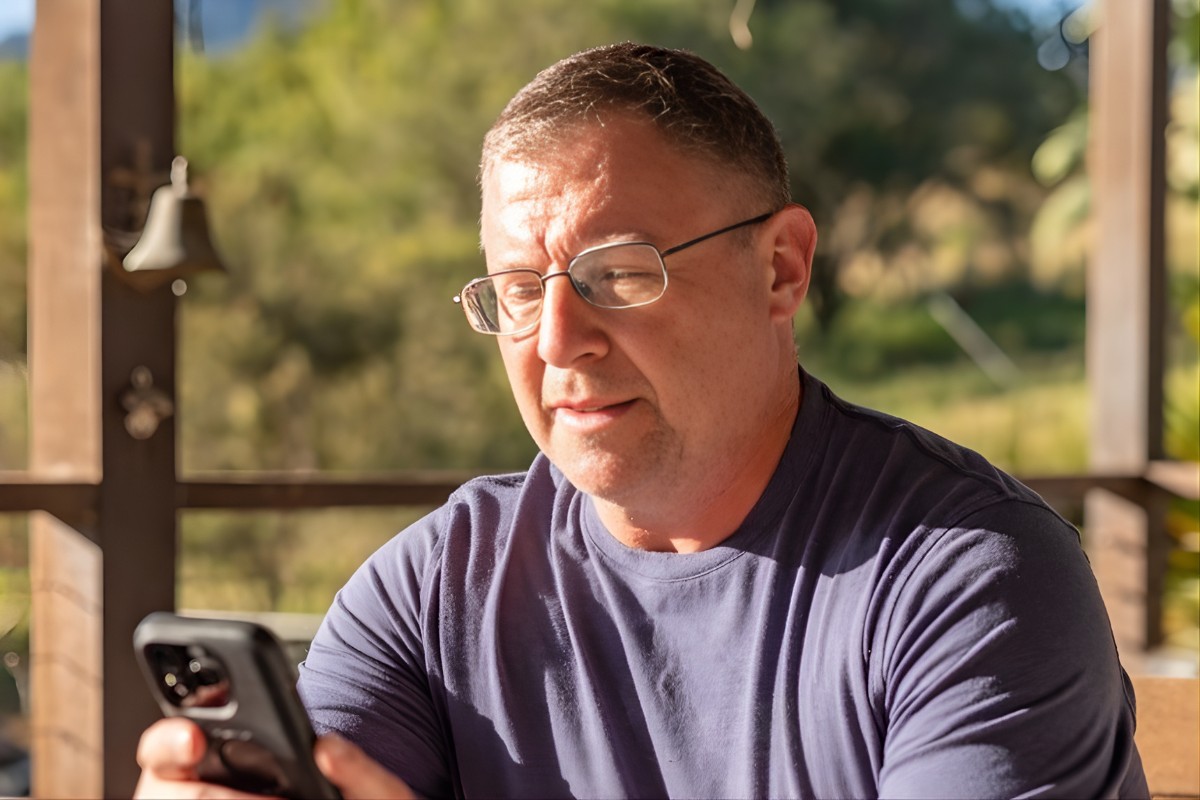 Image of man working from home looking at mobile device sitting outside.
