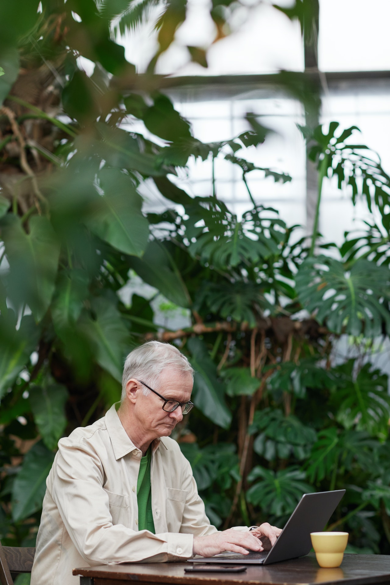 Older man sitting outside working on laptop and drinking coffee